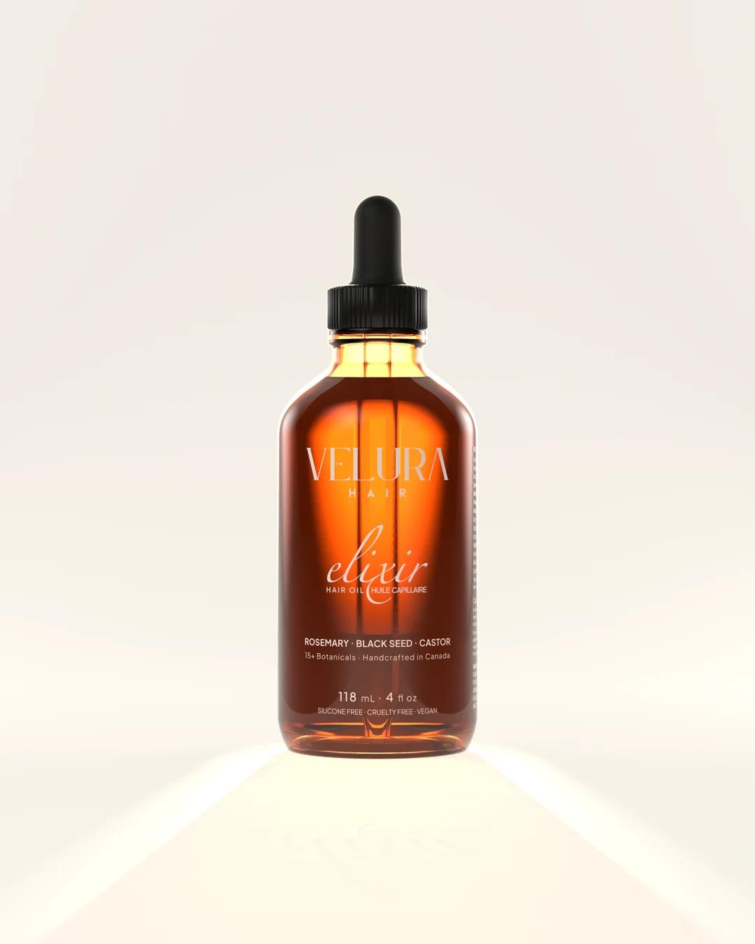 An amber glass bottle of Velura Elixir in a pale studio, lit from behind so the oil glows