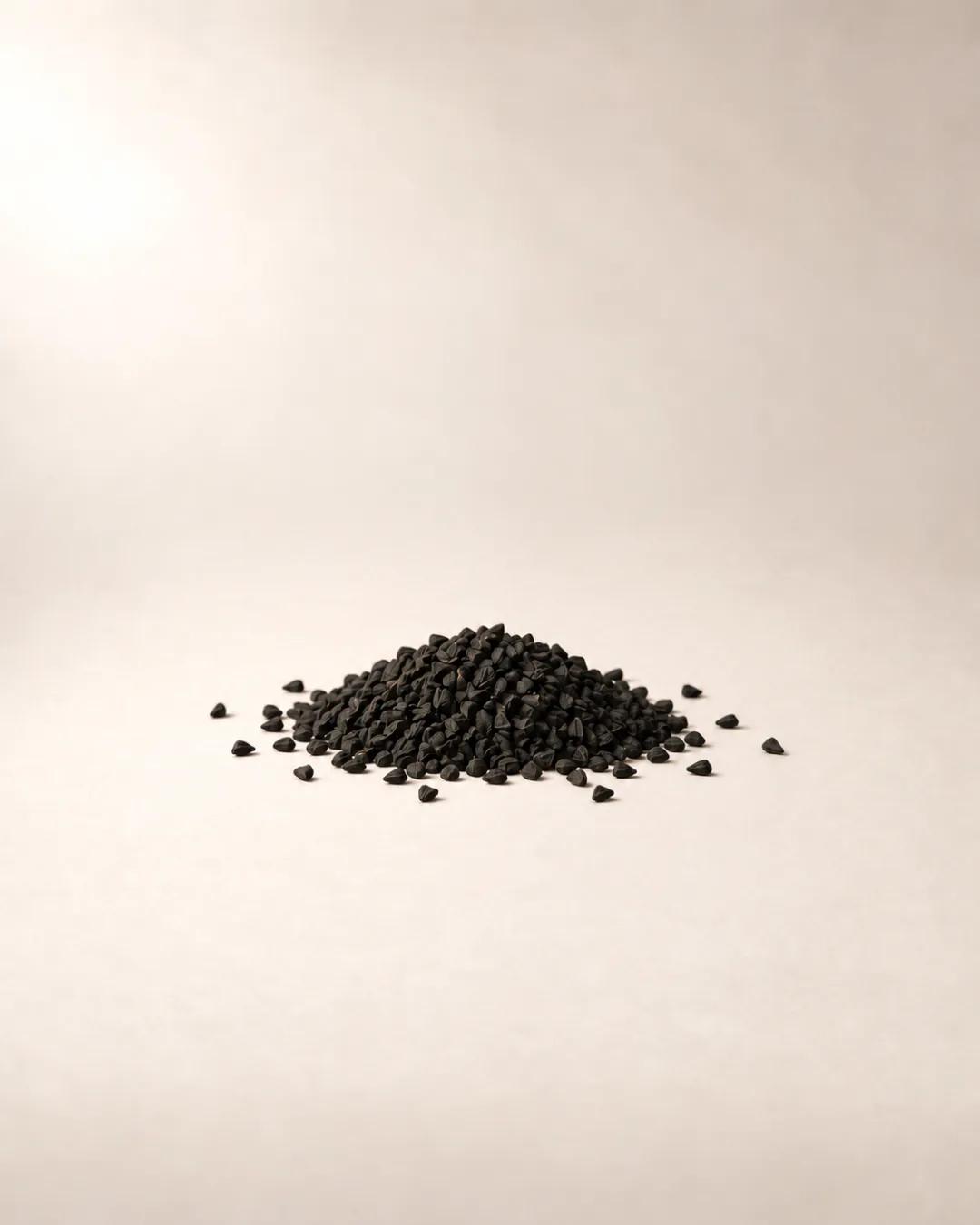 A small mound of matte black nigella seeds on warm off-white paper